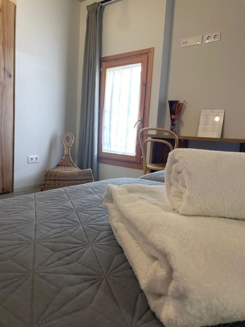 Habitació brillant del L'Algars a Tarragona amb tovalloles enrollades al llit, porta de fusta, escriptori i accés al balcó