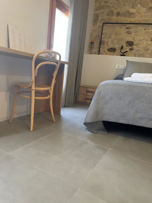 Habitació lluminosa a L'Algars Boutique de Tarragona amb cadira de fusta, llit, escriptori i paret de pedra
