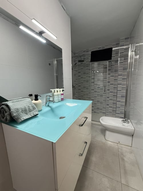 Baño moderno en apartamento de Fuengirola con lavabo turquesa, cabina de ducha cristal e iluminación de espejo
