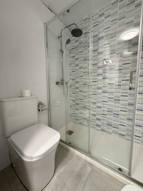 Baño moderno en apartamento de Fuengirola con ducha de cristal, azulejos de rayas, inodoro blanco e iluminación empotrada