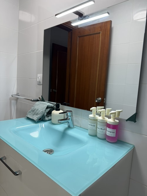 Baño moderno con lavabo turquesa, iluminación LED, espejo, toallas y artículos de tocador en apartamento de Fuengirola