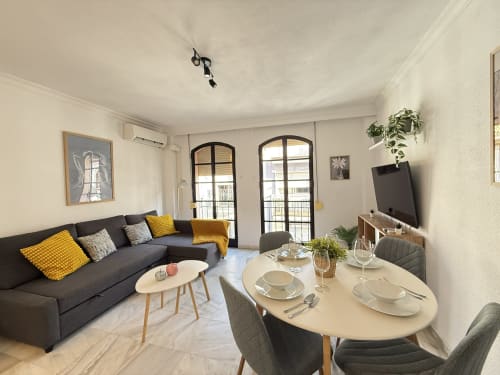 Moderno apartamento en Fuengirola con sofá oscuro, zona de comedor, puertas al balcón y vistas a la ciudad