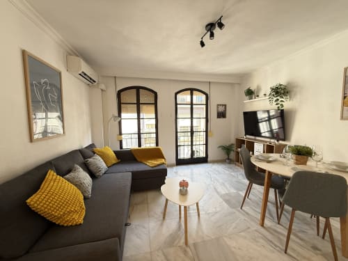 Moderno apartamento en Fuengirola con sofá gris, acentos amarillos, zona de comedor y balcón con vistas a la ciudad