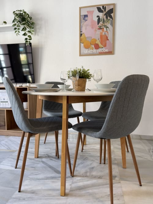 Comedor moderno en apartamento de Fuengirola con mesa redonda, sillas grises y mesa servida con vistas a la sala de estar.