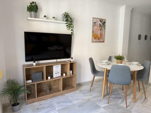 Área de estar de apartamento moderno en Fuengirola con televisor de pantalla plana, mesa de comedor, almacenamiento de madera y plantas en macetas