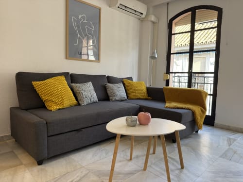 Elegante salón moderno en Fuengirola con sofá gris, detalles en amarillo, mesa redonda y vistas a balcón