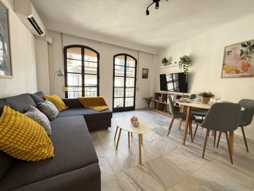 Moderno salón en Fuengirola con sofá gris, detalles amarillos, muebles de madera y puertas balconeras con vistas a la ciudad