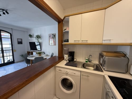 Cocina moderna en apartamento de Fuengirola con lavadora, electrodomésticos de acero inoxidable y vista al salón abierto