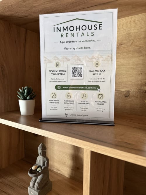 Cartel promocional de Inmohouse Rentals en apartamento de Fuengirola con planta suculenta y figura de Buda en estante de madera