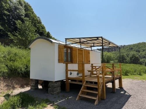 Cabane blanche avec terrasse en bois et pergola aux Cabanes du Nideck, nichée dans un paysage verdoyant près d'Oberhaslach, France