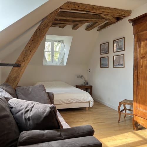 Chambre rustique sous les combles avec poutres apparentes, canapé, lit, vue sur jardin et mobilier en bois aux Anciennes Écuries
