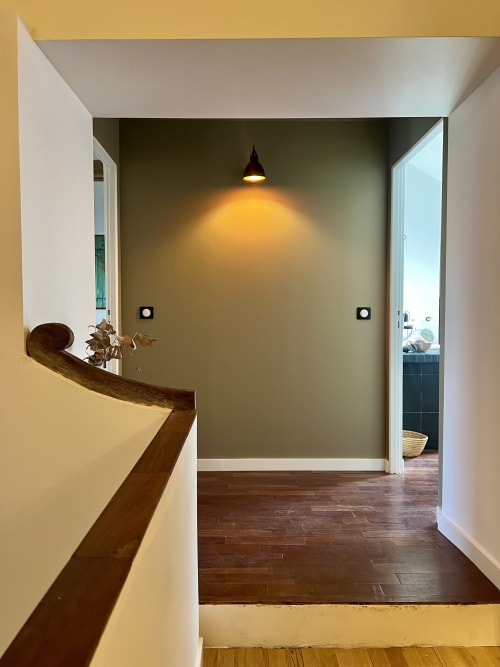 Couloir contemporain avec rampe d'escalier en bois, mur d'accent vert olive et luminaires suspendus aux Écuries du Château