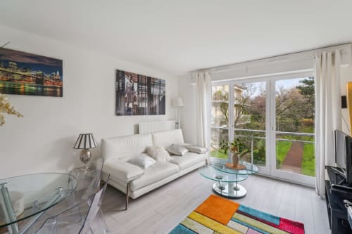 Appartement lumineux et contemporain à la Résidence Aurmat à Boulogne : canapé blanc, table basse en verre, tapis coloré, vue sur le jardin