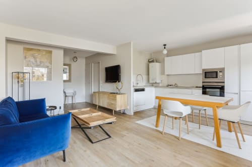 Appartement moderne ouvert à la Résidence Aurmat avec canapé bleu, table en bois et cuisine blanche à Boulogne-Billancourt