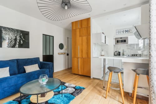 Appartement parisien moderne à la Résidence Aurmat avec canapé bleu, armoire en bois, cuisine blanche et lampe géométrique