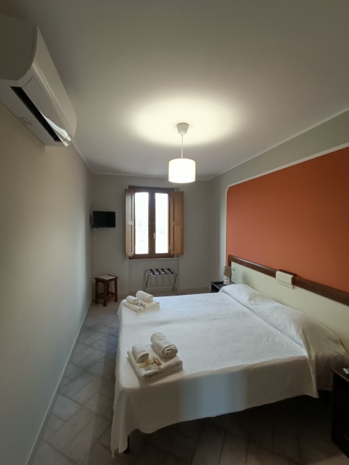 Camera moderna dell'hotel Il Portale a Spinoso con letto bianco, parete accent arancione, lampada a sospensione e climatizzatore