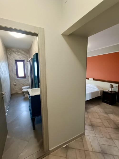 Ingresso camera d'albergo a Il Portale a Spinoso con accesso al bagno, letto con parete accent arancione e comfort moderni