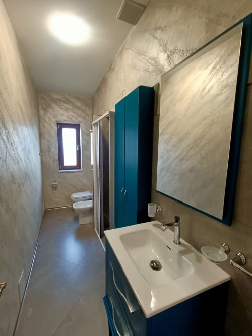 Bagno moderno a Il Portale a Spinoso con vanity blu, lavabo bianco, doccia e specchio turchese