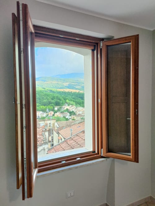 Finestra in legno aperta a Il Portale a Spinoso con vista panoramica sulla valle toscana, tetti e dolci colline verdi