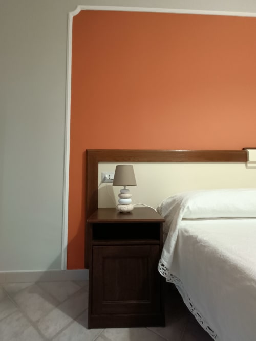 Camera moderna all'hotel Il Portale di Spinoso con parete accent color ruggine, comodino in legno e biancheria bianca