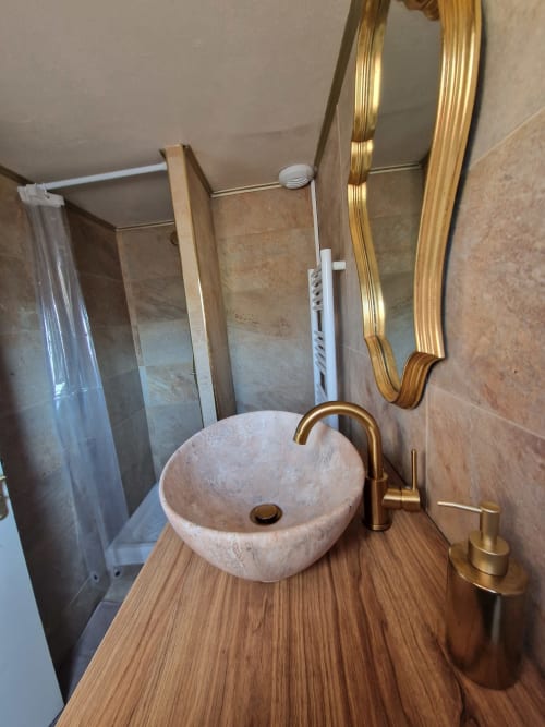 Salle de bain moderne à l'hôtel Accolade à Châteaudun avec vasque en pierre, robinetterie dorée, miroir et douche
