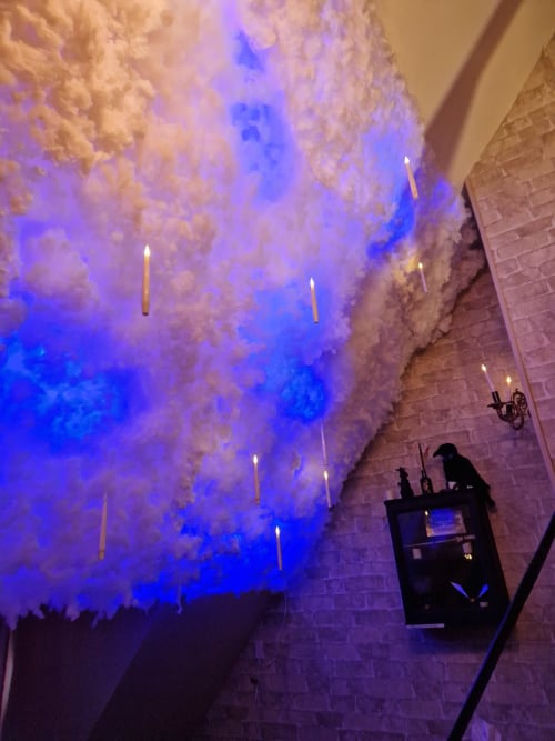 Installation de plafond enchanté avec fleurs blanches flottantes et éclairage bleu dans la salle immersive L'école des sorciers