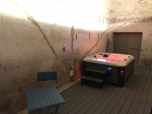 Outdoor hot tub on wooden deck at Les Charmises cottage in Charroux, with blue chair and stone walls