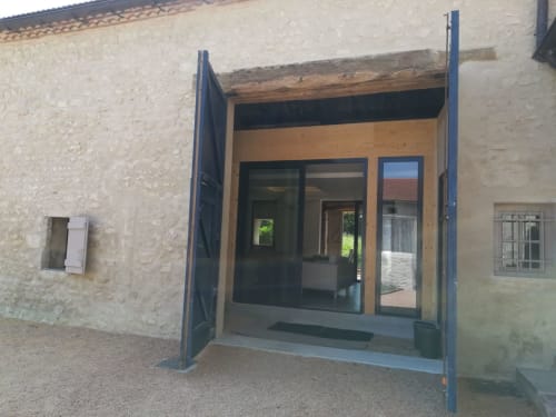 Les Charmises cottage entrance with blue steel frame, wooden accents, and glass doors opening to garden view in Charroux