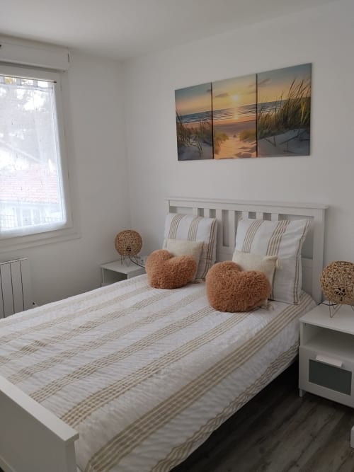 Bright bedroom at La Pause Landaise in Magescq with white bed, striped bedding, decorative cushions, and beach sunset artwork