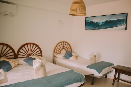 Chambre tropicale Love Rent4 Málaga avec deux lits, têtes de lit en rotin, décor océanique et suspension en fibres tressées