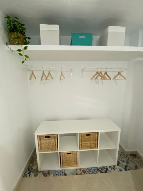 Placard avec étagères blanches, paniers tressés, cintres en bois et plante en pot dans un appartement à Torremolinos