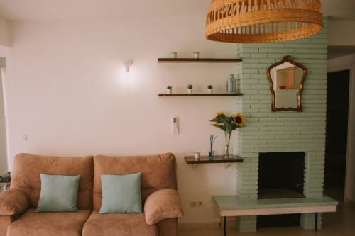 Salon moderne avec canapé en cuir beige, cheminée en briques vertes, suspension luminaire en bois et étagères décoratives chez Love Rent4
