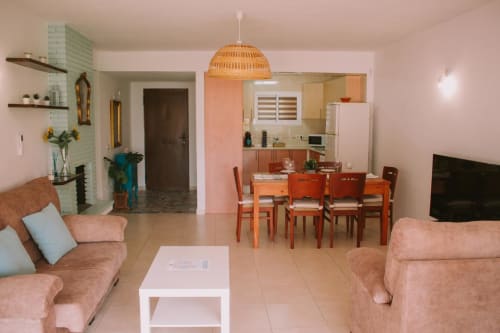 Espace de vie ouvert de l'appartement Love Rent4 à Málaga avec canapés roses, table à manger, cuisine et luminaire suspendu en osier