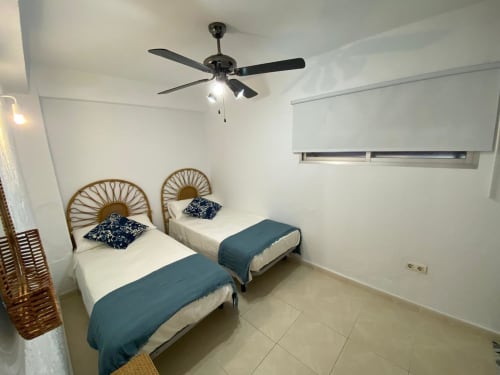 Chambre double avec têtes de lit en rotin, parure bleue et ventilateur de plafond dans l'appartement Love Rent4 de Málaga, Torremolinos