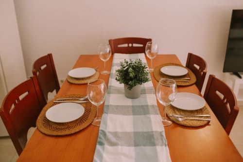 Espace repas à Love Rent4 Málaga avec table en bois, chaises rouges, couverts dressés et plante verte en décoration centrale