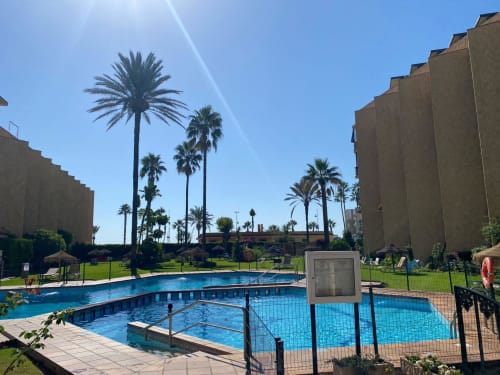 Complexe résidentiel de Torremolinos avec deux piscines entourées de palmiers et jardins verdoyants sous un ciel bleu
