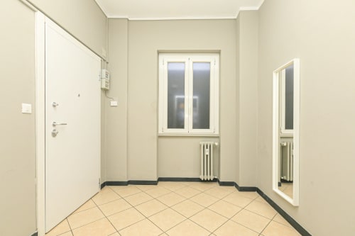 Ingresso luminoso dell'appartamento Rosa House a Genova con pavimento piastrellato, porta bianca, finestre e radiatori
