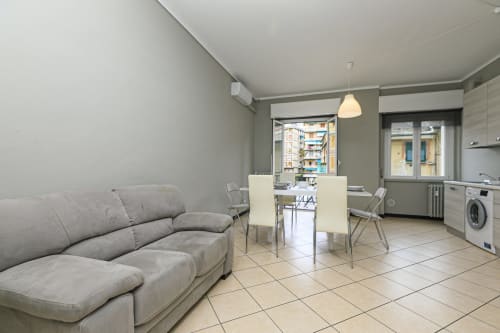 Moderno appartamento a Genova con divano grigio, tavolo da pranzo, cucina e vista sulla città dal balcone