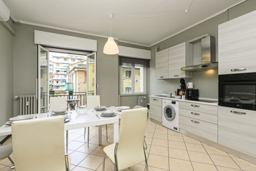 Cucina e sala da pranzo dell'appartamento moderno di Genova con armadiatura bianca, tavolo da pranzo e accesso al balcone con vista sulla città