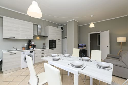 Cucina open space moderna e zona living dell'appartamento Rosa House a Genova, con mobili bianchi e tavolo da pranzo