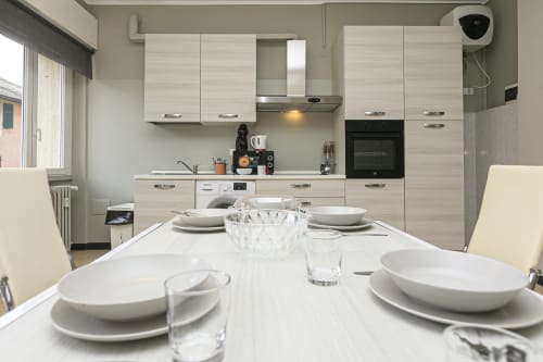 Cucina-sala da pranzo moderna nell'appartamento Rosa House a Genova, con mobili bianchi, tavolo apparecchiato e vista città