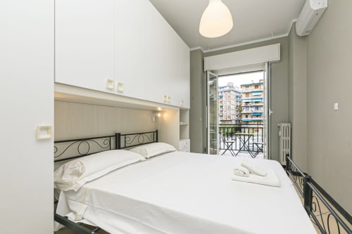 Camera da letto moderna con biancheria bianca, letto in ferro nero e balcone con vista sulla città a Genova, Rosa House