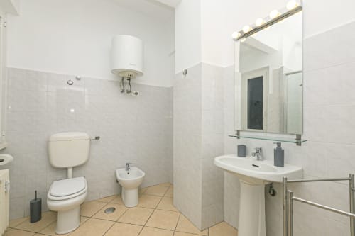 Bagno moderno nell'appartamento Rosa House a Genova, con sanitari bianchi, pareti piastrellate, lavabo su colonna, wc e specchio