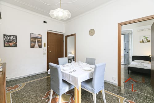 Sala da pranzo della Narciso House con tavolo preparato, sedie bianche e accesso alla camera da letto nell'appartamento di Genova