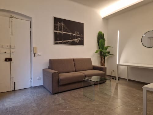 Soggiorno moderno nell'appartamento di Genova con divano marrone, tavolo in vetro, pianta e quadro del ponte illuminato