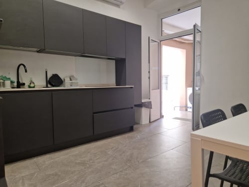 Moderna cucina e zona pranzo dell'appartamento Fresia House a Genova, con mobili neri, elettrodomestici in acciaio inox e legno