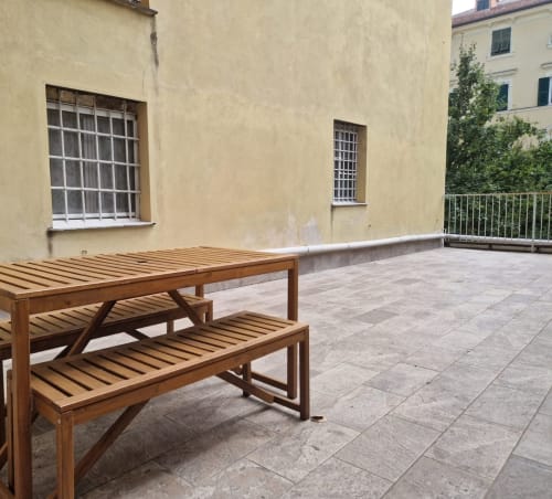 Tavolo da picnic in legno sulla terrazza piastrellata dell'appartamento Fresia House a Genova, con facciata gialla e vista sulla città