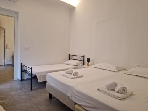 Camera da letto luminosa a Genova con tre letti singoli, biancheria bianca, asciugamani e piccola lampada sul comodino