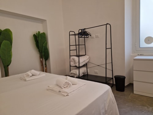 Camera minimalista presso ML White House a Genova con letto, asciugamani, pianta verde, appendiabiti nero e vista sulla città