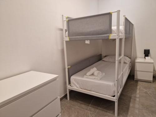 Letto a castello moderno con biancheria grigia nell'appartamento Fresia House, Genova. Struttura bianca con sponde di sicurezza e asciugamani ripiegati al piano inferiore
